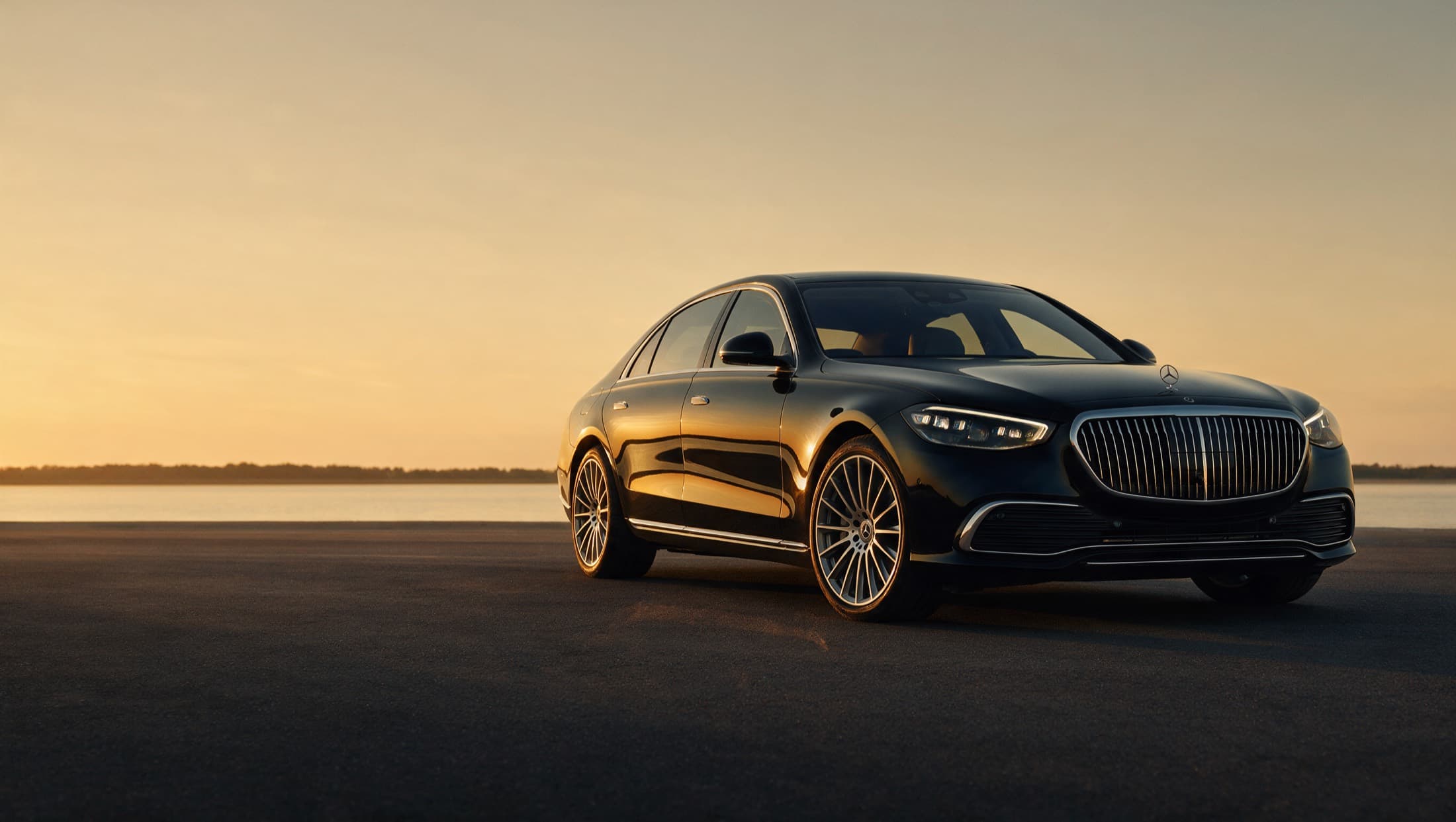 A black Mercedes-Maybach S-Class sedan on an open road at sunset